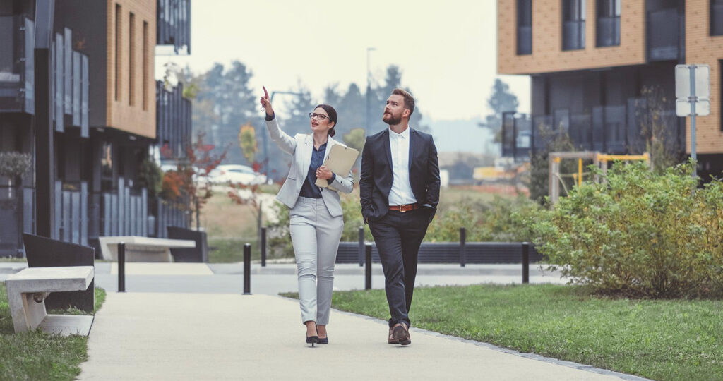 Two people walking in the middle of a luxury apartment complexes explaining the benefits of hiring a property management agency.