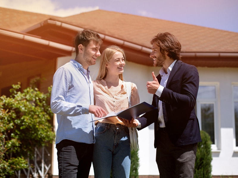 A property management agent assists a couple outside a house