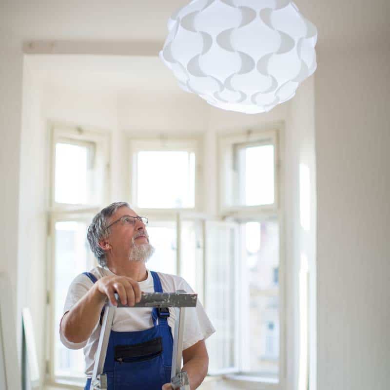 A man standing in front of a white light fixture, highlighting the importance of property maintenance.