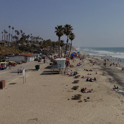 A vibrant beach scene in Oceanside, CA, featuring people enjoying the sun and a colorful kite soaring in the sky.