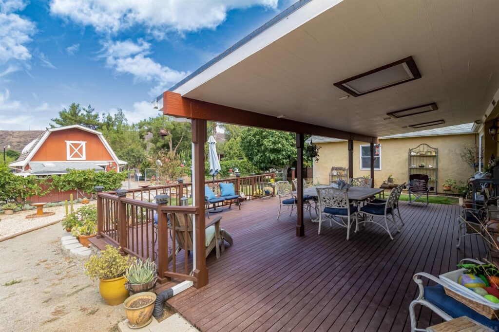 A covered porch featuring a table and chairs, part of a family townhouse with a barn in Ramona, CA.