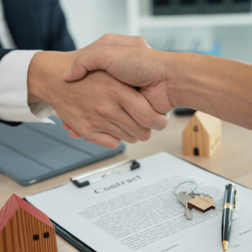 a handshake between two individuals with a contract, a key and a pen on the background.