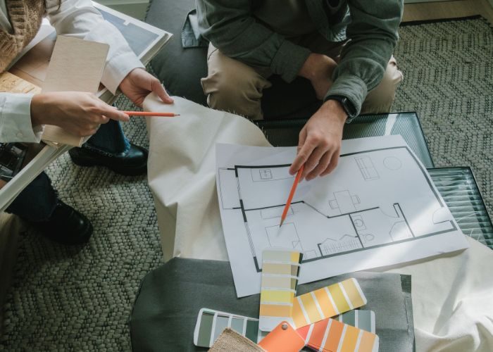 A pair on a sofa with a blueprint and paint, managing property maintenance.