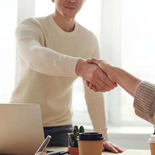 A man and woman shake hands at a desk after closing a real estate deal.